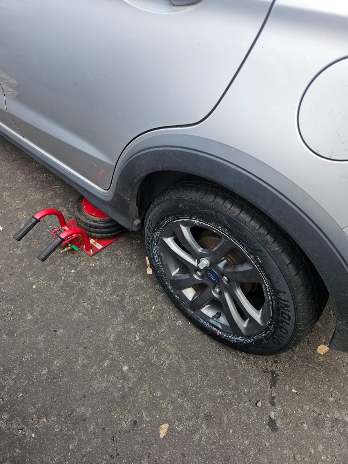 Mobile tyre fitter repairing flat tyre on Ford car at customer location in Glasgow