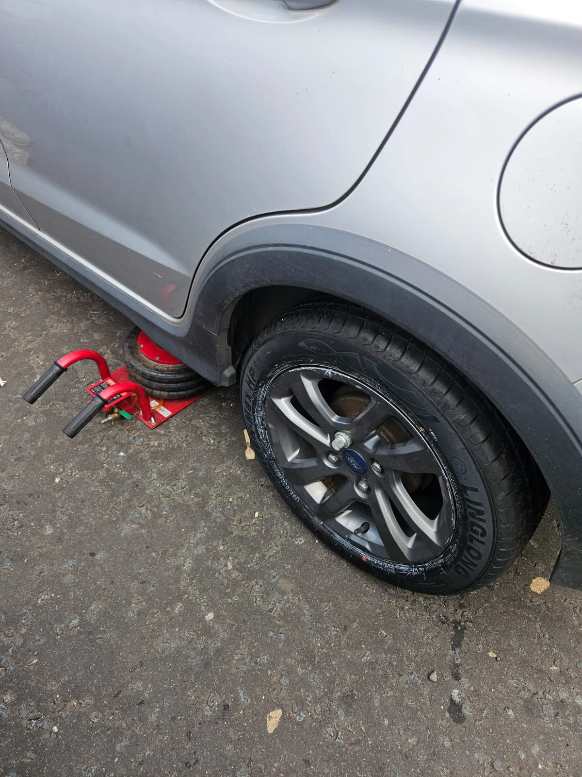 Mobile tyre fitter repairing flat tyre on Ford car at customer location in Glasgow